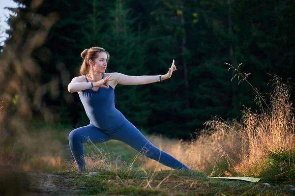 Sporty woman practicing yoga in forest. Middle-aged female exercising early in morning. Female doing sport outdoor.