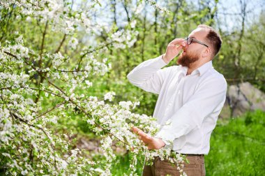 Baharda baharda çiçek açan bahçede mevsimsel alerji yüzünden acı çeken bir adam. Gözlüklü genç adam hapşırıyor, çiçek açan ağacın önünde el pençe divan duruyor. Bahar alerjisi konsepti