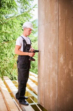 Marangoz ahşap çerçeveli ev inşa ediyor. Evin ön cephesini çimento parçacıkları ile kaplayan işçi onları tornavidayla bağlıyor. Modern çevre dostu yapı kavramı.