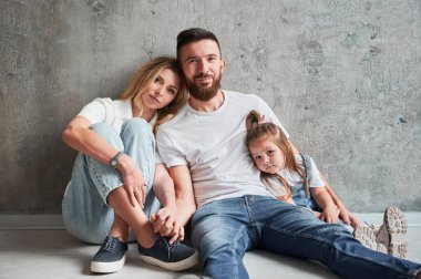 Sevgi dolu ebeveynler ve yeni apartmanın duvarında oturan küçük bir kız. Kadın ve erkek el ele tutuşup kameraya bakarken yeni evinde kızına sarılıyorlar..