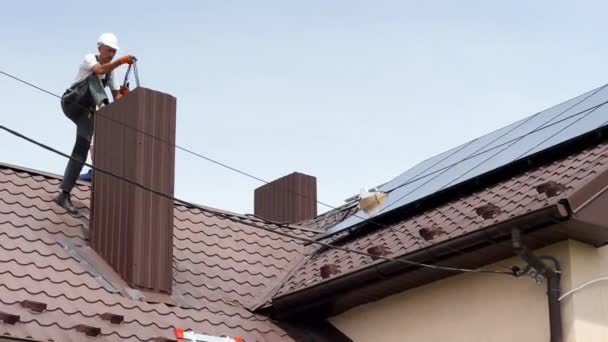 在房顶安装太阳能电池板系统的工人 通过烟囱将太阳能组件电缆与逆变电源连接起来的电工 通过光伏发电 — 图库视频影像