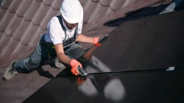 Evin çatısında fotovoltaik güneş paneli inşa eden bir işçi. Güneş modülünü takan eldivenlerdeki adam mühendis hex anahtarı yardımıyla dışarı çıkıyor. Alternatif ve yenilenebilir enerji üretimi kavramı.
