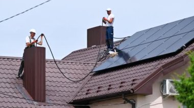 İşçiler evin çatısına güneş panelleri kuruyor. Fotovoltaik etki yoluyla elektrik üretmek için güneş modüllerinden bacaya kablolar bağlayan elektrikçiler.