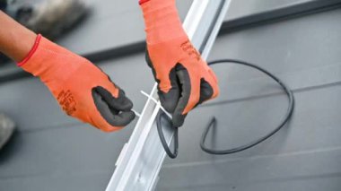 İşçi fotovoltaik etkiyle elektrik üretmek için evin çatısına güneş panelleri kuruyor. Elektrikçi, kabloları özel bir kravatla güvene alıyor. Yenilenebilir enerji kavramı.