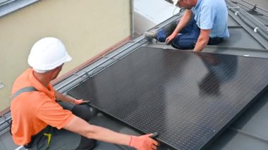 İşçiler evin çatısına fotovoltaik güneş paneli inşa ediyorlar. Miğferli teknisyenler ve eldivenli adamlar dışarıda büyücülerin yardımıyla güneş modülü kuruyorlar. Yenilenebilir enerji üretimi kavramı.