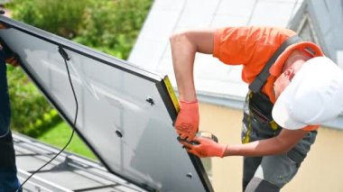 Fotovoltaik etkilerle elektrik üretmek için evin çatısına güneş paneli inşa eden işçiler. Kurulum için montaj ekipmanlarını ölçmek için cetvel kullanan adam.