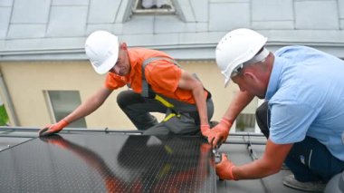 İşçiler evin çatısına fotovoltaik güneş paneli inşa ediyorlar. Miğferli teknisyenler ve eldivenli adamlar dışarıda büyücülerin yardımıyla güneş modülü kuruyorlar. Yenilenebilir enerji üretimi kavramı.