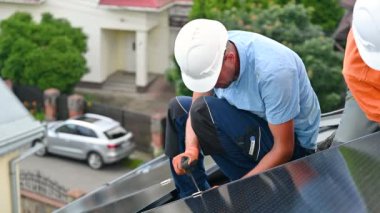 Evin çatısında fotovoltaik güneş paneli inşa eden bir işçi. Miğferlerde mühendis ve eldivenler dışarıda altıgen anahtarla güneş modülü kuruyor. Alternatif enerji üretimi kavramı.