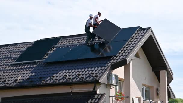 在房顶上建造太阳能电池板系统的工人 两名戴钢盔的男子在室外安装光电太阳能组件 绿色和可再生能源发电概念 — 图库视频影像