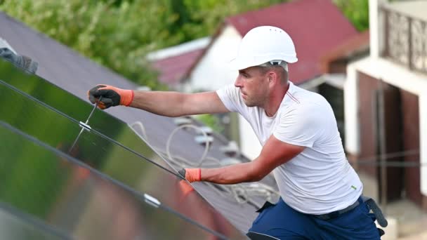 工人在房顶上建造光伏太阳能电池板系统 戴着头盔和手套的男子工程师在室外用六角钥匙安装太阳能组件 替代能源生产概念 — 图库视频影像