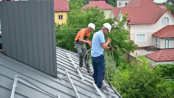在房顶安装太阳能电池板系统的男工 戴钢盔的电工在室外用绳索提起光伏太阳能组件 替代能源和可再生能源的概念 — 图库视频影像