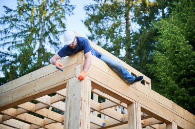Marangoz ormanın yakınında iki katlı ahşap çerçeve inşa ediyor. Gözlüklü sakallı adam koruyucu kask takarak çivi çakıyor. Günümüz ekolojik yapısı fikri