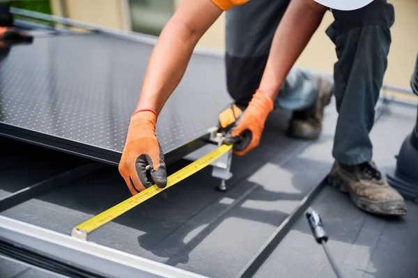 Worker building solar panel system on rooftop of house for generating electricity through photovoltaic effect. Close up man using ruler to measure mounting equipment for precise installation.