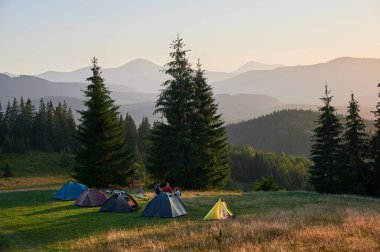Dağlarda kamp yapmak için iyi akşamlar. Bir grup genç turist kamp alanındaki çadırlarda yürüyüş yaptıktan sonra dinleniyor ve günbatımının keyfini çıkarıyorlar. Turizm, seyahat ve yürüyüş kavramı.