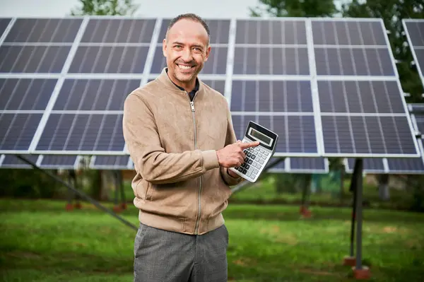 Smiling man showing future income from investing in alternative energy. Happy man demonstraiting big number on calculator. Man glad about huge sum profit.