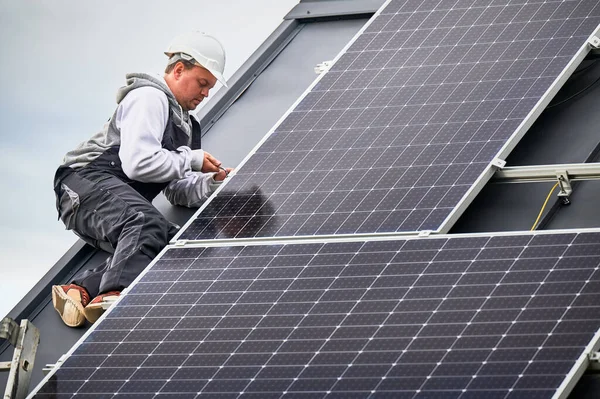 男工在房顶上安装光电太阳能电池板 头盔工程师用六角钥匙安装太阳能模块系统 可再生能源的替代概念 免版税图库图片