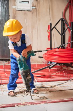 Çocuk inşaat işçisi daireye ısıtma sistemi kurarken sondaj makinesi kullanıyor. Güvenlik kasklı çocuk tadilat sırasında evde elektrikli çekiçle sondaj yapıyor..