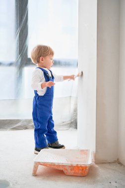 Boya fırçasıyla duvar boyayan tamirci çocuk. İş yerindeki çocuk evde oynarken boya fırçası kullanıyor..