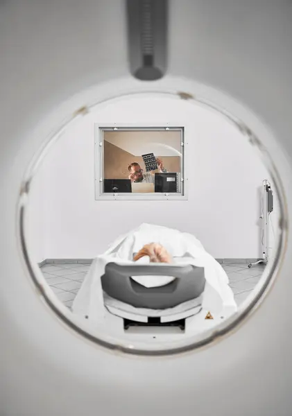 Medical computed tomography or MRI scanner. Doctor examining MRI results, female patient lying on couch. Concept of modern diagnostics.