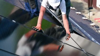 Evin çatısında fotovoltaik güneş paneli inşa eden bir işçi. Güneş modülünü takan miğferler ve eldivenler içindeki insan mühendislerine açık alandaki hex anahtarının yardımıyla yaklaşın. Alternatif enerji.