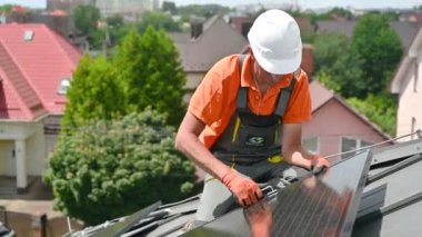 Evin çatısında fotovoltaik güneş paneli inşa eden bir işçi. Miğferlerde mühendis ve eldivenler dışarıda altıgen anahtarla güneş modülü kuruyor. Yenilenebilir enerji üretimi kavramı.