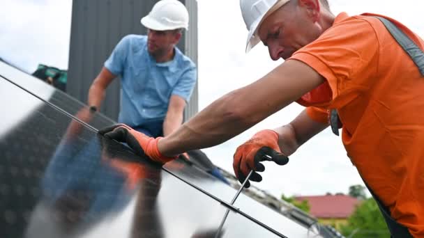 在房顶上建造光伏太阳能电池板系统的工人 戴着头盔和手套的男性技术人员在室外用六角钥匙安装太阳能组件 替代能源生产概念 — 图库视频影像