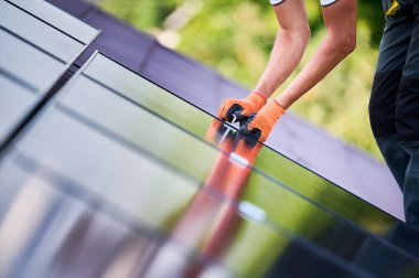 Evin çatısında fotovoltaik güneş paneli inşa eden bir işçi. Eldiven takan insan mühendislerine yakın çekim yapın. Güneş modülü takın. Dışarıdaki hex anahtarının yardımıyla. Yenilenebilir enerji üretimi kavramı.