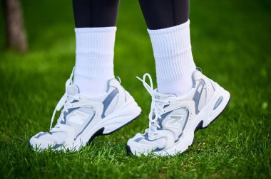 Lviv, Ukrayna - 28 Nisan 2023: aktif yaşam için rahat spor ayakkabıları. Gri koşucular içinde sportif bir kadın ve çimlerin üzerinde beyaz bir çift New Balance 530 spor ayakkabı..
