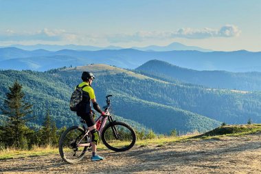 Güneşli bir günde dışarıda bisiklete binen bisikletçi. Erkek turist tepede dinleniyor, güzel dağ manzarasının tadını çıkarıyor, miğfer ve sırt çantası takıyor. Aktif boş zaman kavramı.