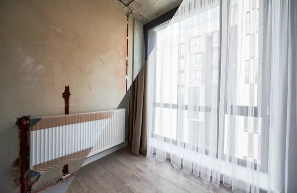 Comparison of apartment flat before and after restoration or refurbishment. Photo collage of old room with large windows and new renovated room with heating radiator, parquet floor and white walls.