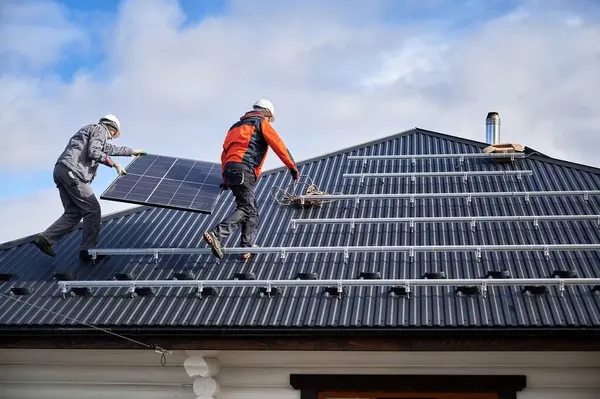 Arbeiter Tragen Solarzellen Auf Einem Hausdach Zwei Ingenieure Installieren Sonnigen lizenzfreie Stockfotos
