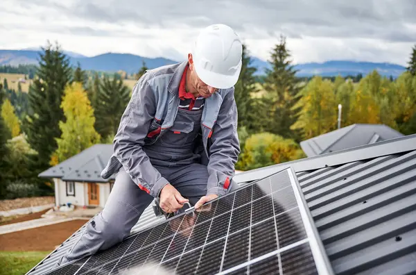 建筑工人在房顶上安装光伏太阳能电池板 头盔工程师用六角钥匙安装太阳能模块系统 可再生能源的替代概念 免版税图库图片