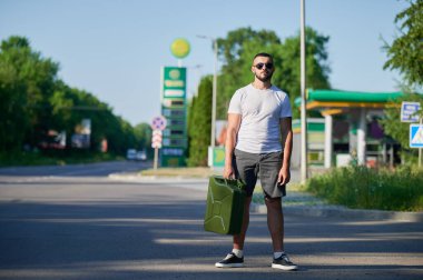 Kendine güvenen adam sonunda benzin istasyonunu buldu ve teneke kutuyu doldurdu. Adam yakıt ikmali için arabaya dönüyor. Benzin istasyonunun arka planında elinde teneke kutuyla genç bir erkek..