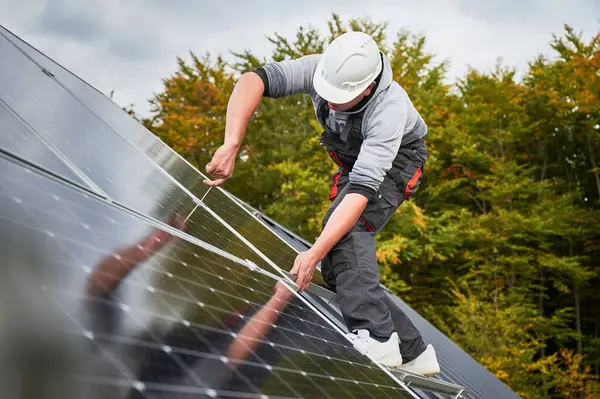 在房顶上安装太阳能光伏电池板的人 头盔工程师用六角钥匙安装太阳能模块系统 可再生能源的替代概念 免版税图库照片