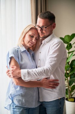 Mutlu çift evde arka planda sarılıyor. Güzel bir kadın gülümsüyor ve kocasına kapalı gözlerle sarılıyor. Sıradan giyinmiş tatlı bir çift..