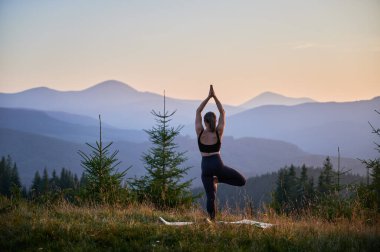 Yoga yapan ve dışarıda, dağlarda meditasyon yapan bir kadın, sakin, doğal bir ortamda. Kadın yoga pozu veriyor paspasın üzerinde, gün doğumunda ya da günbatımında güzel dağ manzarasının arka planıyla.