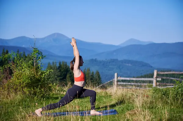 Dağlarda yoga yapan bir kadın, sakin, doğal bir ortamda. Kadın yoga pozu veriyor paspasın üzerinde, gün doğumunda ya da günbatımında güzel dağ manzarasının arka planıyla.