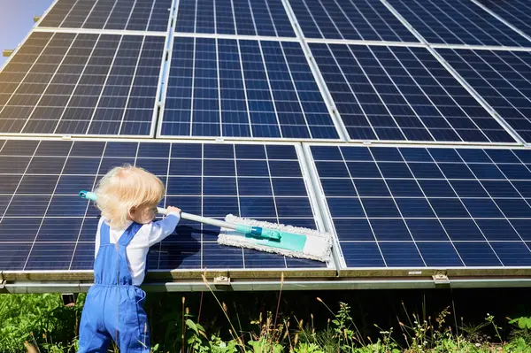 Small boy learning how to care about solar panels. Back view of young kid cleaning new solar battery at warm sunny day. Concept of young generation and alternative energy.