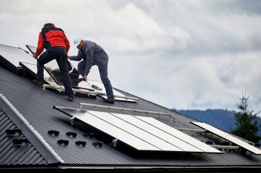 Atçılar evin çatısına güneş paneli inşa ediyorlar. Dışarıda fotovoltaik güneş modülü taşıyan miğferli işçiler. Alternatif ve yenilenebilir enerji kavramı.