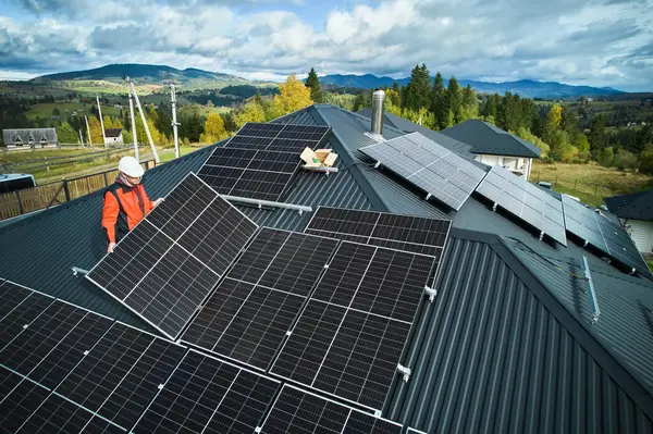 技术人员在房顶上建造光伏太阳能模块站 在室外安装太阳能电池板系统的头戴钢盔的男性屋顶 替代能源和可再生能源的概念 空中景观 免版税图库照片