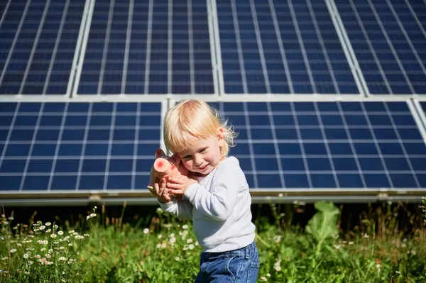 Child trying to find out how much money is in his piggy bank on background of solar panels. Small kid learning about saving money for future. Concept of saving money, investment in renewable energy.