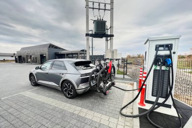 Ivano-Frankivsk, Ukrayna - 24 Ekim 2023: Modern elektrikli araç Hyundai şarj istasyonunda. Aracın arkasında iki elektrikli dağ bisikleti taşıyan bisiklet parkı var..