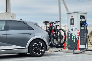 Ivano-Frankivsk, Ukraine - October 24, 2023: Cropped view of modern electric vehicle at charging station. Mounted on back of vehicle is bike rack carrying two electric mountain bicycles. clipart