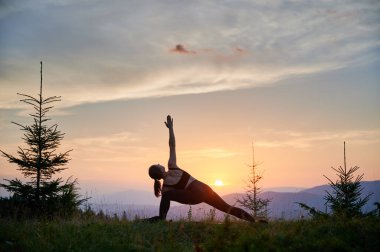 Dağlarda yoga yapan bir kadın, sakin, doğal bir ortamda. Yoga yapan kadın, gün doğumunda ya da günbatımında güzel dağ manzarasının arkaplanıyla.