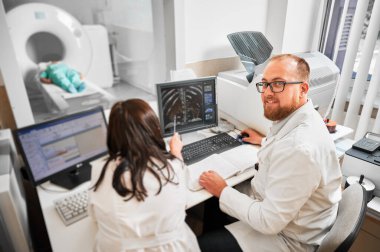 Tıbbi bilgisayarlı tomografi ya da MRI tarayıcısı. Doktorun portresi, bilgisayarda çalışmak, MR sonuçlarını hemşireyle incelemek. Beyaz cüppeli uzmanlar, danışmanlık. Tıp kavramı.