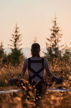 Lotus pozisyonunda oturan sportif kızın arka görüntüsü. Genç bir kadın, dağları gören bir yerde yoga yapıyor. Gündoğumunda meditasyon.