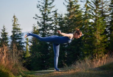 Ormanda yoga yapan orta yaşlı bir kadın. Savaşçı 3 pozu veren sportif bir kadın. Şafakta jimnastik yapıyorum..