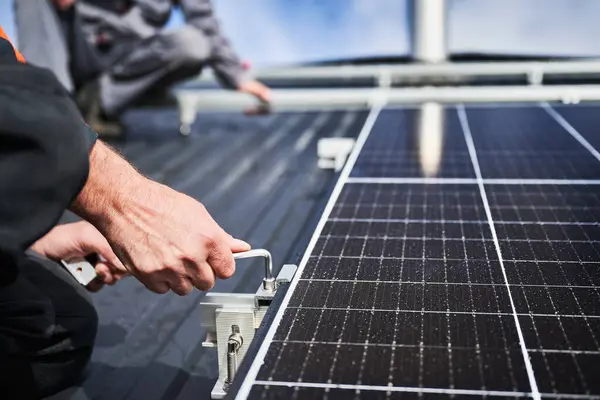 Man engineer mounting photovoltaic solar panels on roof of house. Close up view of technician installing solar module system with help of hex key. Concept of alternative, renewable energy.