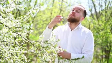 Tıbbi göz damlası kullanan alerjik bir adam baharda çiçek açan bahçede mevsimsel alerjiden muzdarip. Açık havada çiçek açan ağacın önünde gözleri tedavi eden yakışıklı bir adam. Bahar alerjisi konsepti.