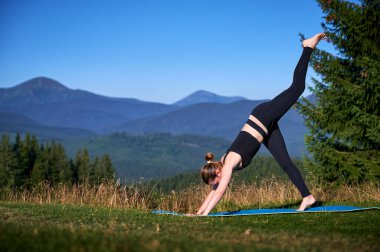 Dağlarda yoga yapan bir kadın, sakin, doğal bir ortamda. Kadın yoga pozu veriyor paspasın üzerinde, gün doğumunda ya da günbatımında güzel dağ manzarasının arka planıyla.